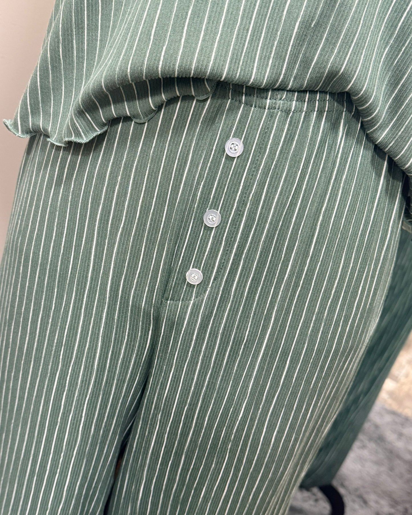 Green pinstripe pajama pants with buttons on a neutral background