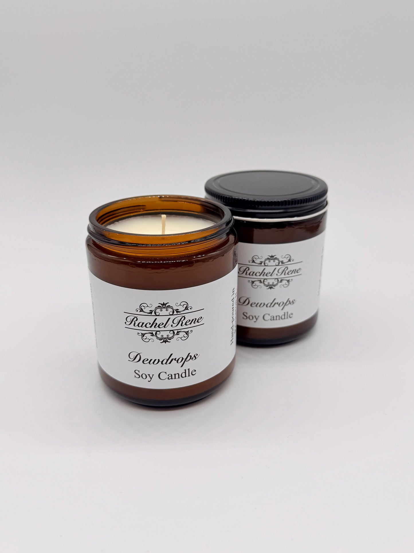 Two dewdrops soy candles in amber jars with labels on a white background