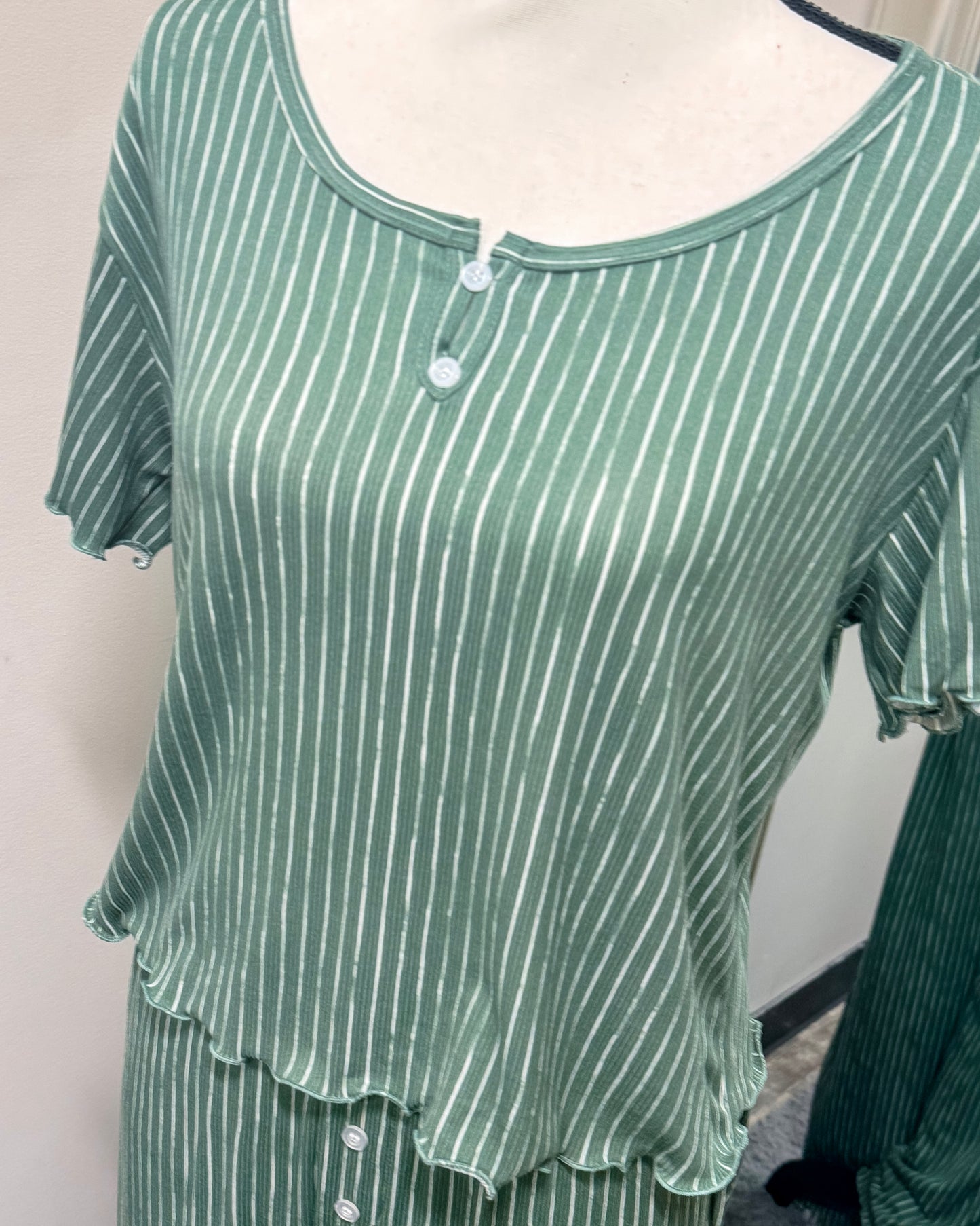 Green and white striped pajama shirt with small button on neckline on a mannequin against a plain background