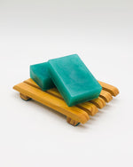 Two semi-transparent rectangular teal soap bars on a wooden soap dish.