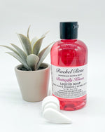 A pink Butterfly Kisses liquid soap with a black pull-top cap. A white pump lies to the left.