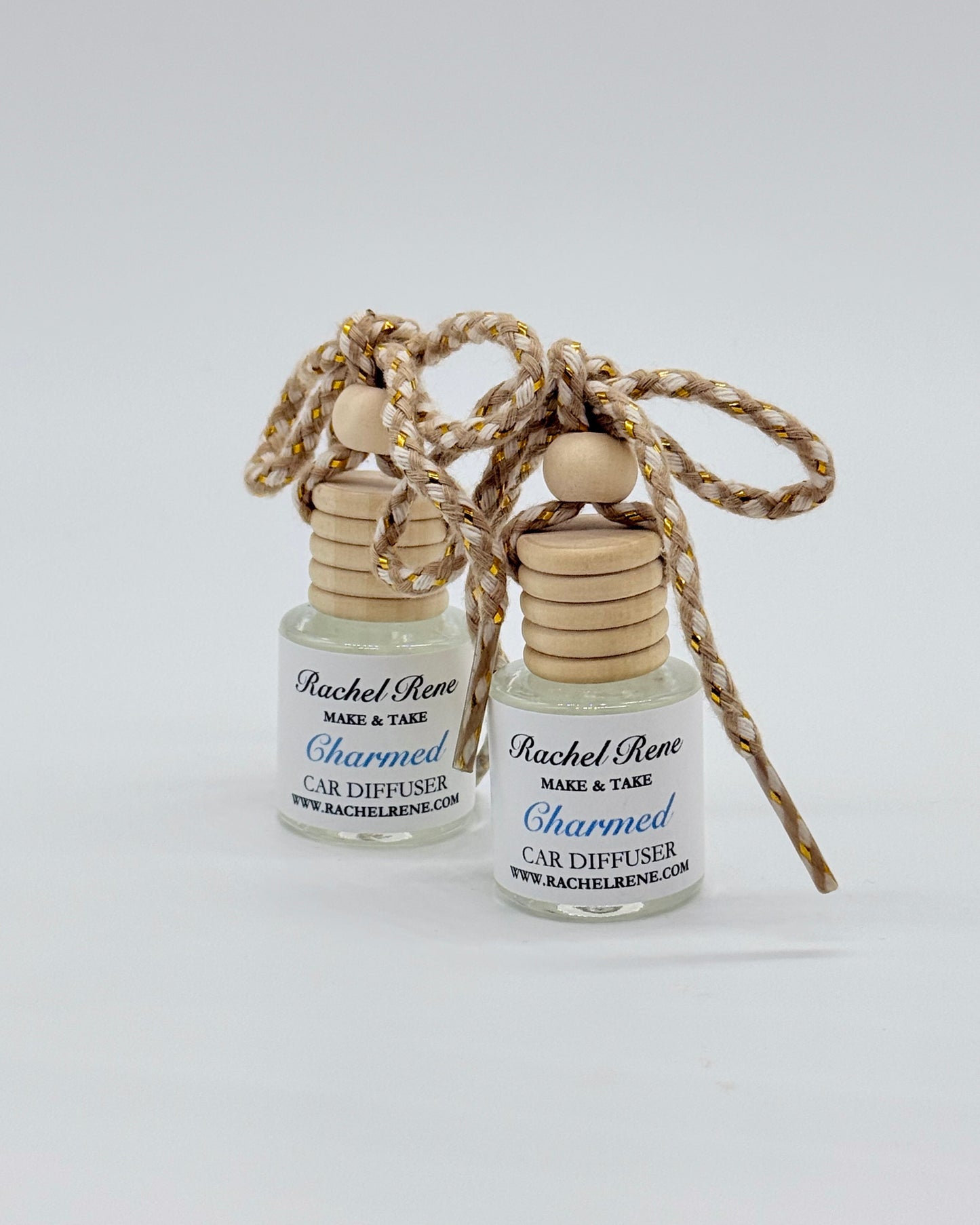 Two bottles of Rachel Rene Car Diffuser with wooden tops and braided string on a white background