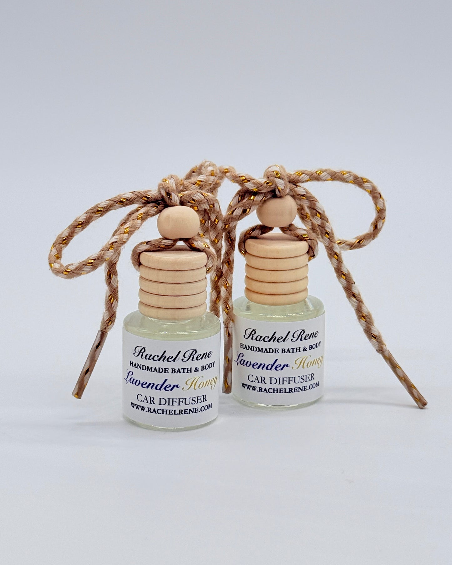 Two bottles of Rachel Rene Car Diffuser with wooden tops and braided string on a white background
