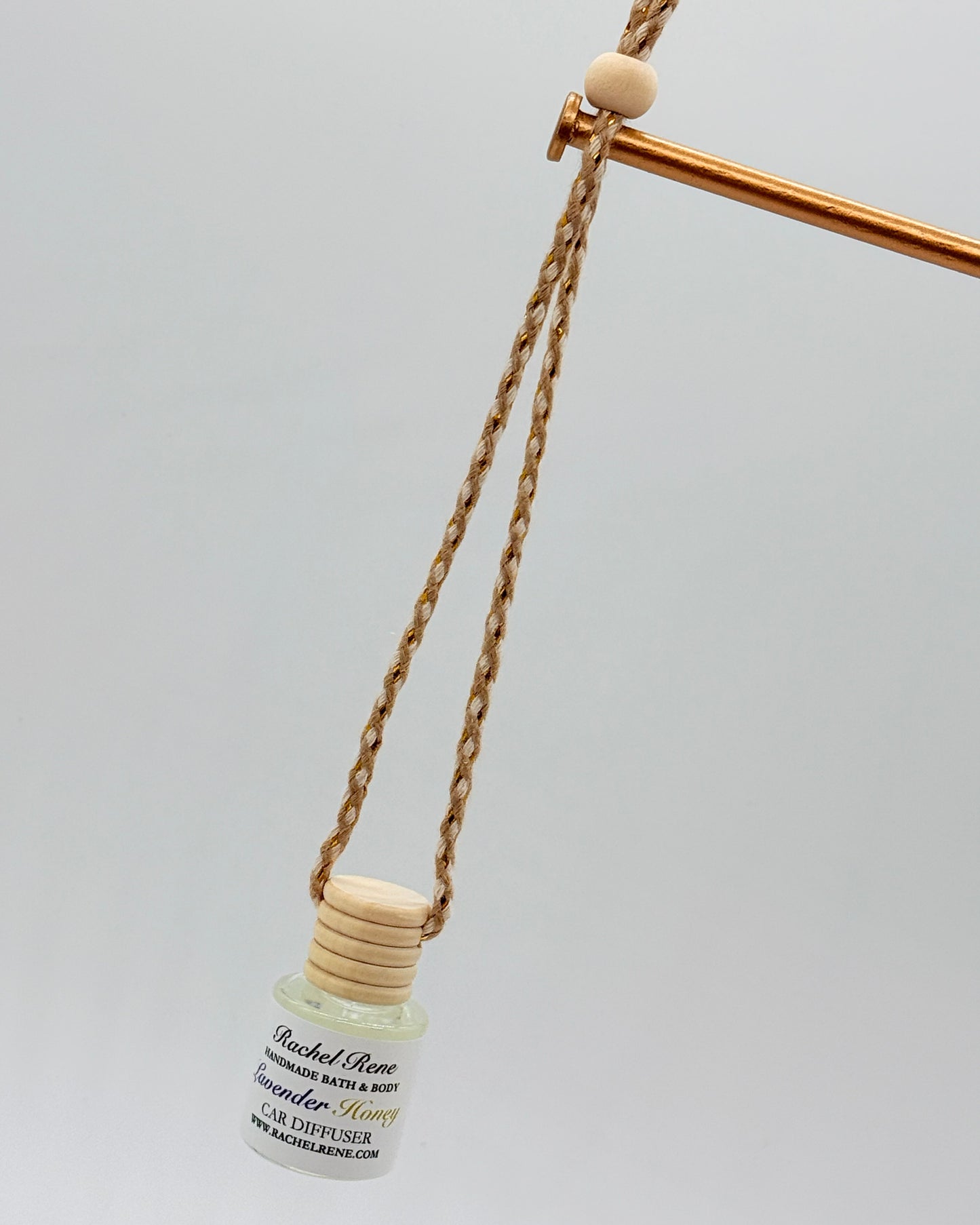 Car diffuser with a wooden top hanging from a braided rope string on a light gray background