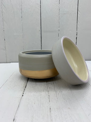 A gray ceramic wax warmer with a gold band on the bottom. The top cup is detached and leaning against the base.